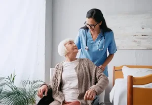 happy nurse in eyeglasses moving aged woman in wheelchair