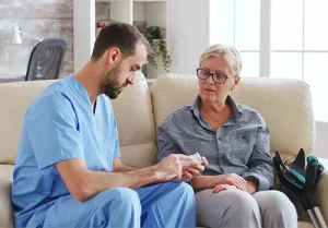Male nurse sitting on couch with senior woman giving her medical treatment in her home.