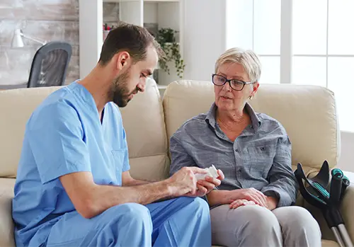 Male nurse sitting on couch with senior woman giving her medical treatment in her home.