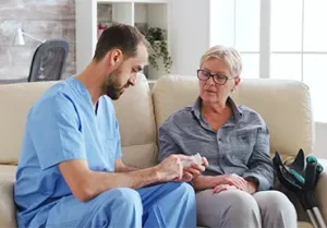 Male nurse sitting on couch with senior woman giving her medical treatment in her home.