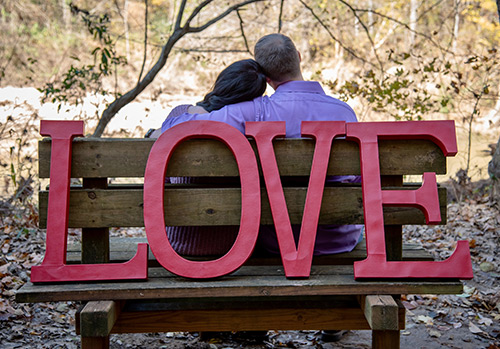 Large red letters spelling out love are photographed with a couple sitting behind the sign.