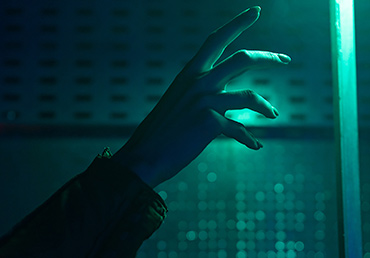 An green-colored artificial light source reveal's a woman's hand reaching out.