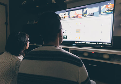 A couple sits in the dark and searching for something to watch together on TV. 