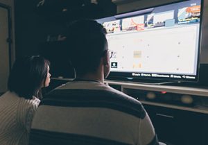 A couple sits in the dark and looks for something to watch on TV.