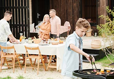 A family prepares for an outdoor barbecue meal.