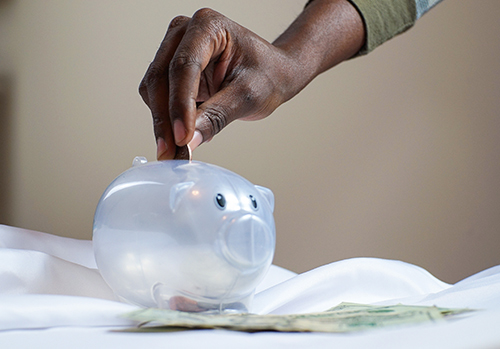 A hand is seen dropping a coin into a translucent piggy bank.