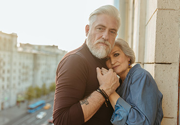A senior couple hold hands while standing on a balcony.