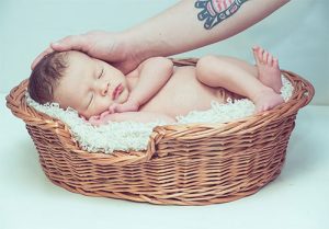 Photo of a baby in a cradle with a parent's hand