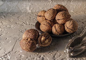 Several walnuts sit in a bowl next to a nutcracker.