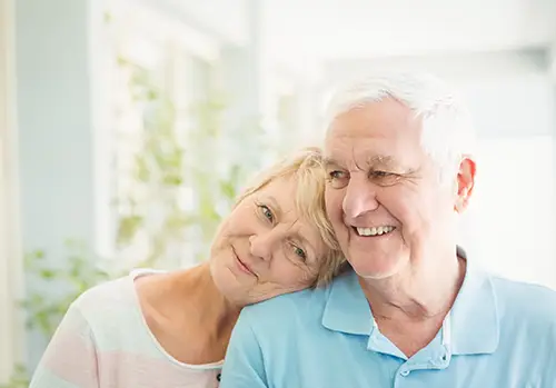 Medicare eligible older couple smile together as they cuddle.