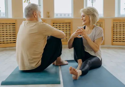 An older couple sit on exercise mats and smile.