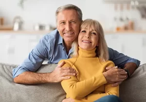Happy Senior Couple Embracing Sitting On Sofa At Home
