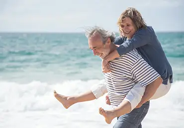 A happy wife is carried by her smiling husband as he walks on the beach shore.