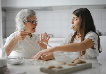 Grandmother and granddaughter having an engaging conversation while baking cookies together in a bright, modern kitchen.