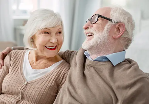 Older man and woman sit on couch laughing.