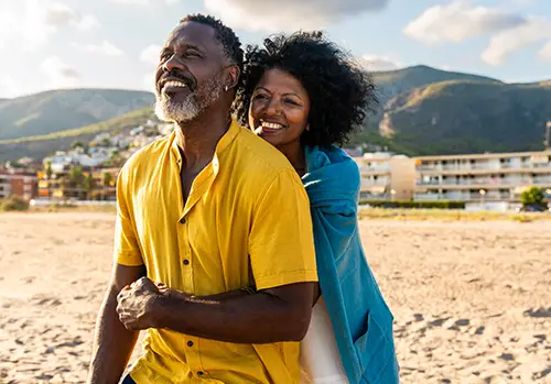 A husband and wife hug each other on the beach.