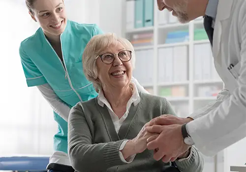 A smiling woman shaking a doctor's hand and another nurse is smiling.