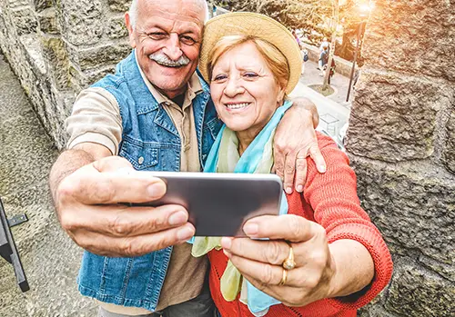 Older couple smiling at phone while taking selfie as they are traveling with their Medigap plan.