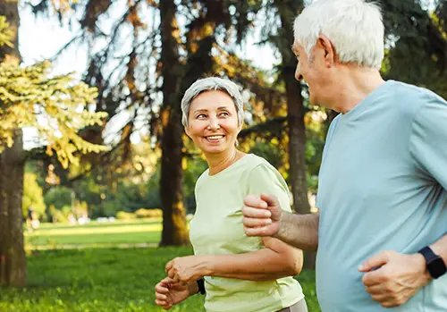 A senior couple jogs together in the park.