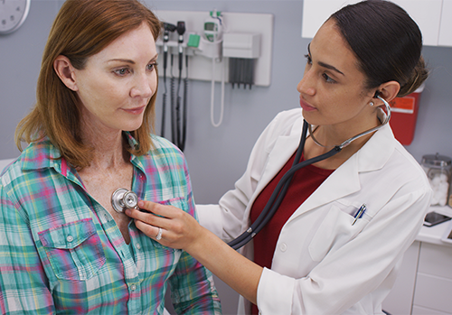 short term health coverage pros and cons woman and doctor at office performing check up on patient Large