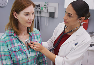 short term health coverage pros and cons woman and doctor at office performing check up on patient Thumbnail