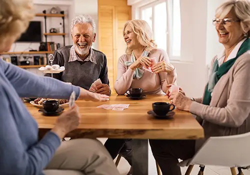 Group of seniors sits around a table and plays cards while laughing.
