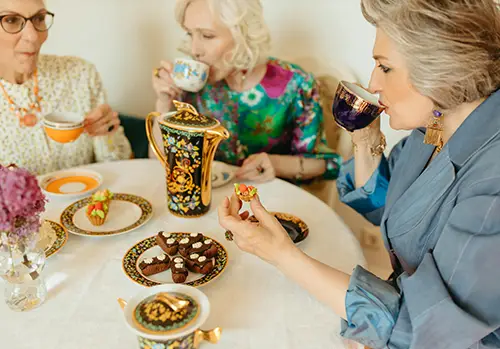 Three ladies drinking tea and eating snacks at a party.