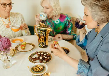 Three ladies drinking tea and eating snacks at a party.