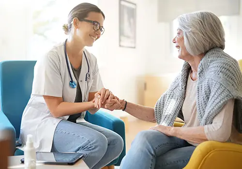 Doctor and older woman sit together and hold hands at her appointment.