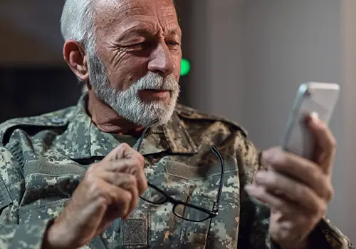 An elderly veteran man looks at his cell phone.