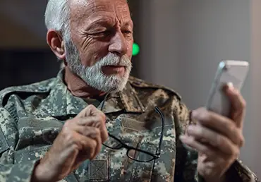 An elderly veteran man looks at his cell phone.