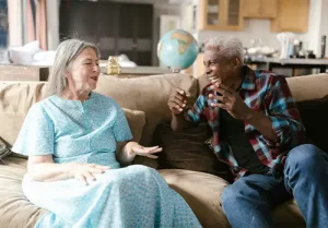Senior couple sitting on a cozy sofa, smiling and laughing together as they discuss Medicare and possible supplement coverage.