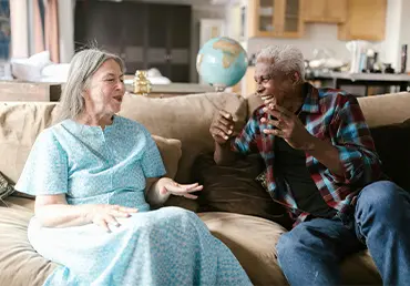 Senior couple sitting on a cozy sofa, smiling and laughing together as they discuss Medicare and possible supplement coverage.