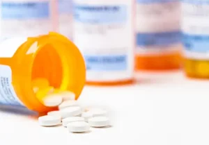Round white prescription medication medicine pill tablets spilling from a bottle with numerous full bottles in background
