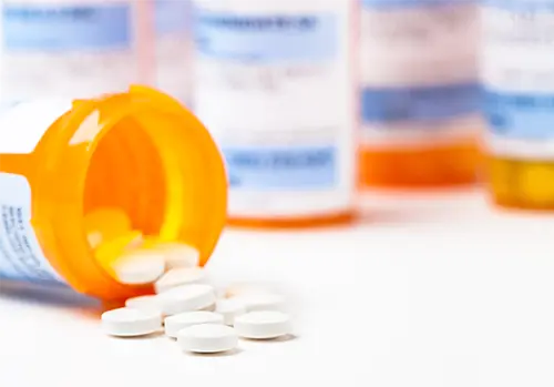 Round white prescription medication medicine pill tablets spilling from a bottle with numerous full bottles in background