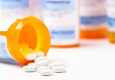 Round white prescription medication medicine pill tablets spilling from a bottle with numerous full bottles in background