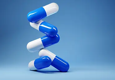 A stack of antibiotic pill capsules on a blue background.